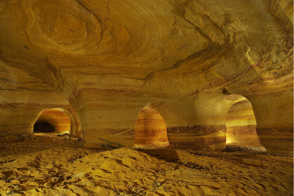 addentrarmi dentro formazioni rocciose: grotte di arenaria screziata più grandi d'Europa, create interamente dall'uomo nel corso dei secoli a causa dell'estrazione di sabbia quarzifera usata per la produzione del vetro. Mi affascina che all'interno spiccano suggestive stratificazioni di sabbia gialla, rossa e arancione, caratterizzate da increspature pietrificate e pattern ondulatori generati dal movimento dell'acqua milioni di anni fa.