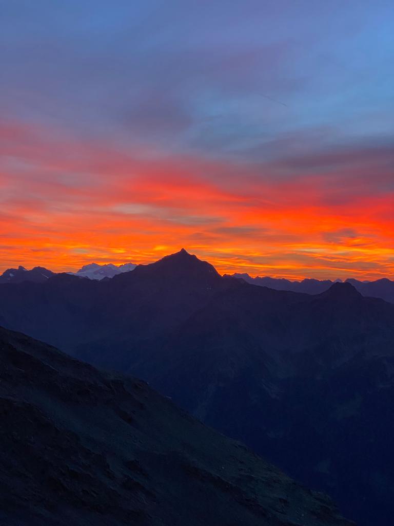 Il silenzio della montagna, i colori e le sfumature intense del tramonto, contemplandoli davanti ad un buon piatto, assaporando un bicchiere di vino rosso come il cielo, accanto a lei.