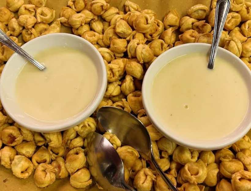 nutrire il corpo, coccolare lo spirito: preparare una pioggia di tortellini e due laghi di fonduta calda, vellutata e specchiante. C'è un'archeologia dei ricordi che si nasconde nei gesti semplici. Questa distesa dorata fatti a mano racconta di domeniche mattina lente, di mani infarinate e di una sapienza tramandata nel tempo. Al centro, le ciotole di fonduta vellutata; non sono un semplice condimento ma un porto sicuro in cui intingere la tradizione. Un invito a rallentare, a sedersi vicini e a ritrovare il benessere nell'abbraccio caldo del cibo di casa.