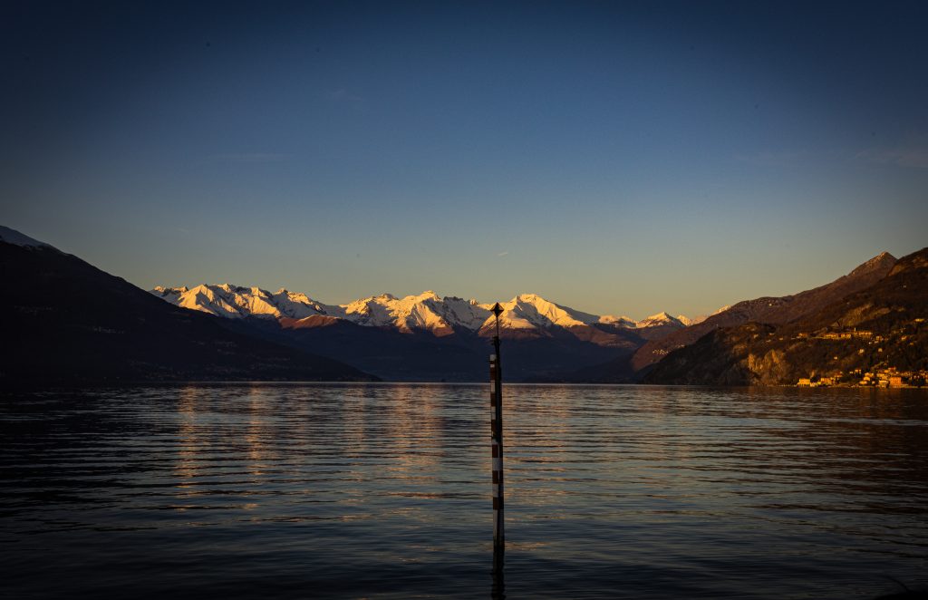 un tramonto invernale guardando le montagne innevate dalla punta che divide il lago di Como in due rami: Como e Lecco.